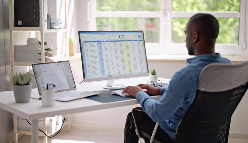 Un homme est assis à un bureau avec son ordinateur portable ouvert et effectue un travail professionnel sur un écran externe avec un clavier externe.