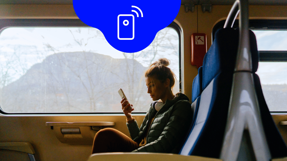 Frau, die im Zug sitzt und auf ihr Handy blickt
